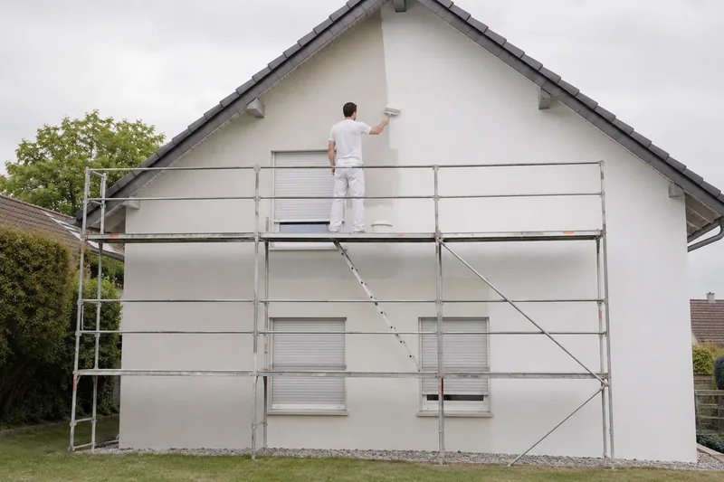 Fassadenanstrich vom Gerüst aus, halb fertige Fassade in gebrochenem Weiß